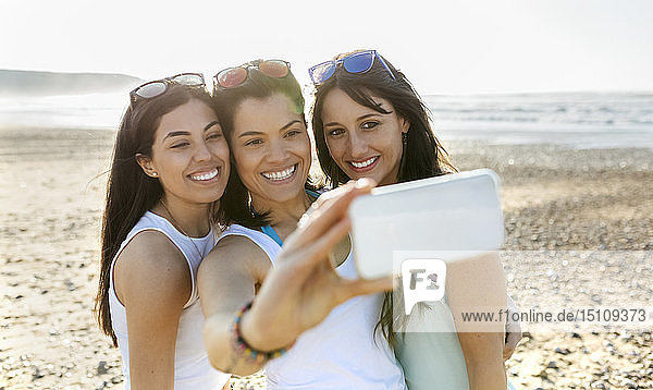 Porträt von glücklichen Freundinnen  die am Strand ein Selfie machen