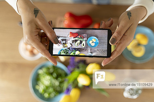 Woman's hands holding smartphone taking picture of vegetables