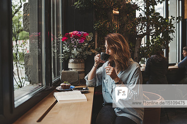 Junge Frau trinkt aus Kaffeetasse in einem Café