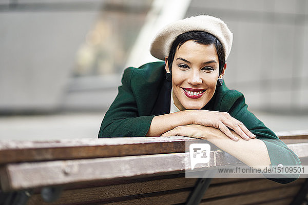 Porträt einer lächelnden  modischen jungen Frau auf einer Bank sitzend