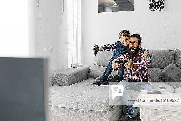 Aufgeregte Vater und Sohn spielen zu Hause Computerspiel