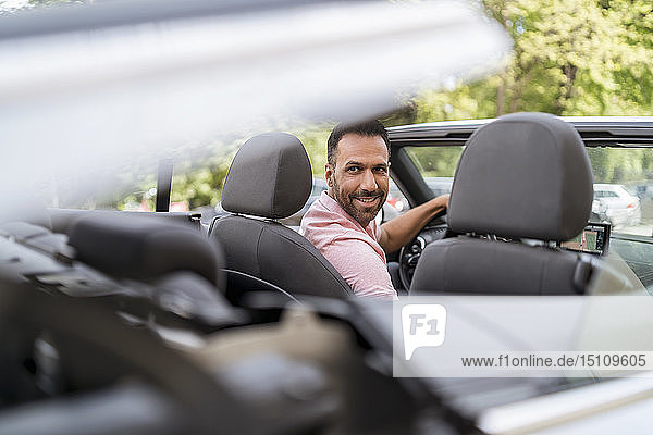 Man sitting in car with closing convertible top
