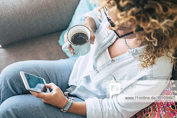 Frau zu Hause auf Couch mit Kaffeetasse und Handy