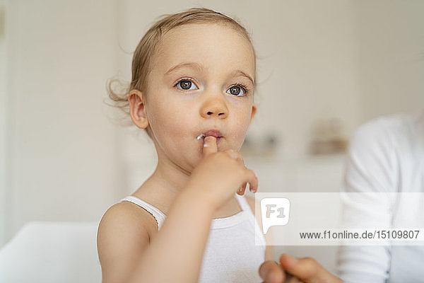 Little girl licking her finger while making a cake in kitchen at home