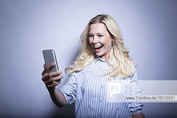 Porträt einer glücklichen blonden Frau beim Betrachten eines Smartphones
