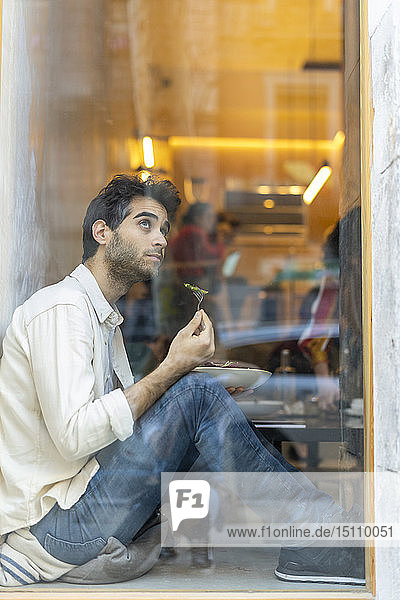 Mann isst einen Salat und sitzt in einem Restaurant am Fenster und schaut hinaus