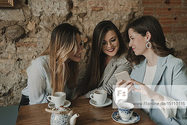Drei junge Frauen  die sich in einem Café ein Handy anschauen