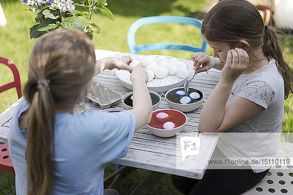 Zwei Mädchen färben Ostereier auf dem Gartentisch