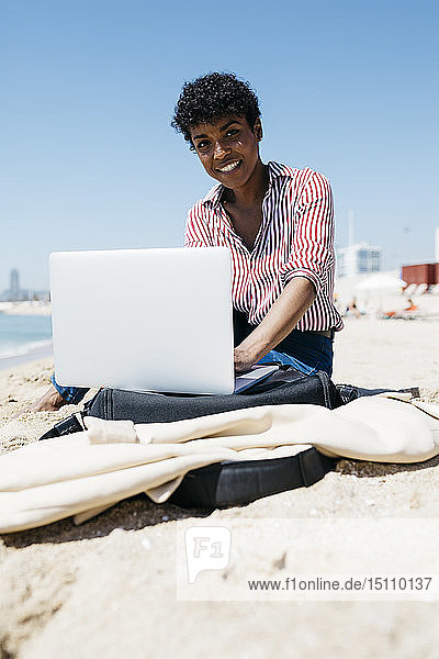 Frau sitzt am Strand  während sie mit dem Laptop arbeitet