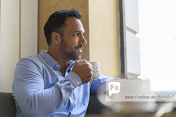 Lächelnder Geschäftsmann mit einer Tasse Kaffee  der aus dem Fenster schaut