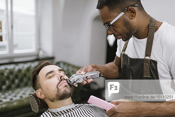 Barber cutting beard of a customer in barber shop
