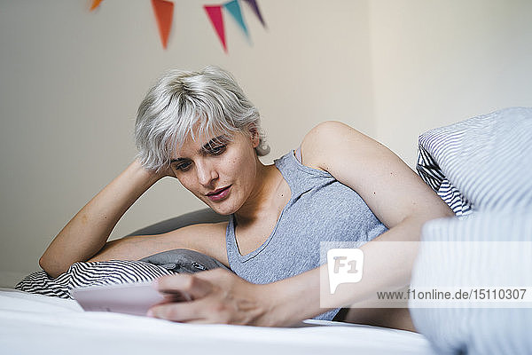 Frau liegt im Bett und benutzt Mobiltelefon