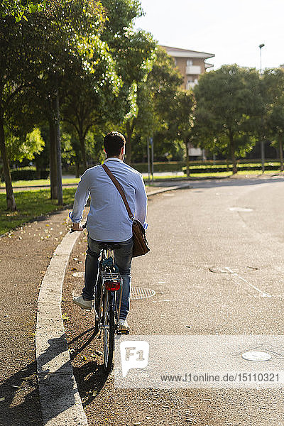 Rear view of young man riding a bicycle on road