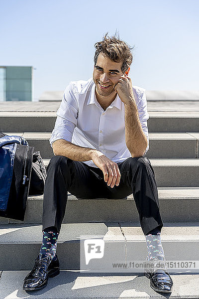 Porträt eines glücklichen Geschäftsmannes  der auf einer Treppe sitzt und eine Pause macht