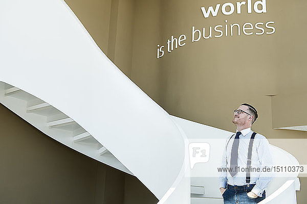 Selbstbewusster Geschäftsmann schaut in einem modernen Büro die Treppe hinauf
