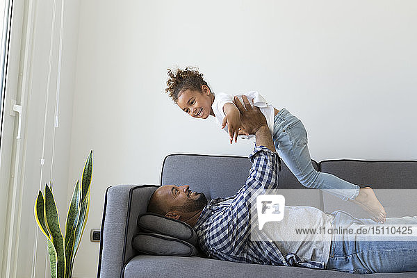 Glückliche Vater und Tochter spielen zu Hause auf der Couch