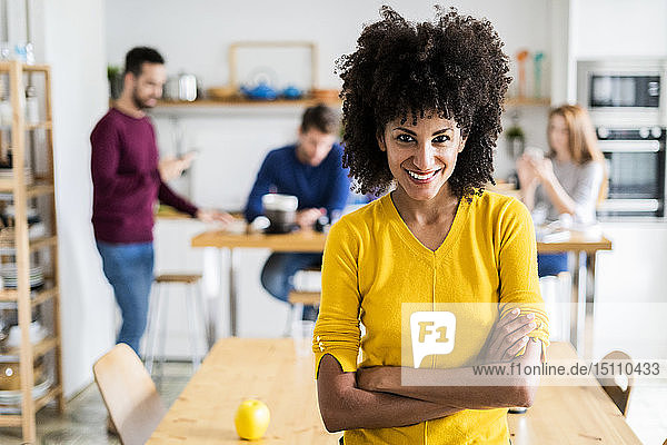 Porträt einer lächelnden Frau am Esstisch zu Hause mit Freunden im Hintergrund
