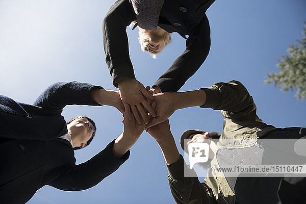 Blick aus der Froschperspektive auf drei Frauen  die ihre Hände unter blauem Himmel stapeln