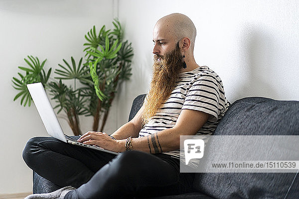 Hipster  der zu Hause auf der Couch sitzt und einen Laptop benutzt