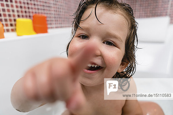 Porträt eines lachenden kleinen Mädchens in der Badewanne  das auf den Betrachter zeigt