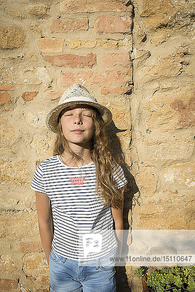 Mädchen mit Strohhut  mit geschlossenen Augen an der Wand lehnend  Toskana  Italien