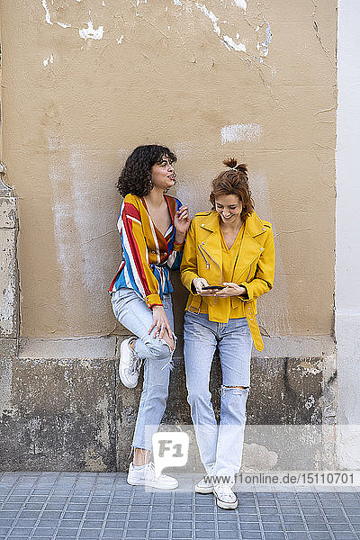 Zwei junge Frauen mit Handy stehen vor einem Gebäude