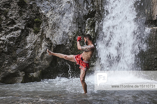 Young man doing boxing workout at a waterfall