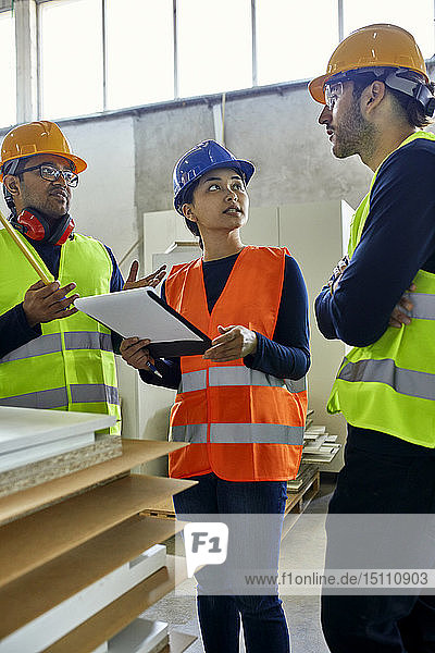 Two men and woman in reflective vests discussing in factory