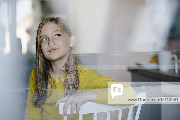 Porträt eines Mädchens  das zu Hause auf einem Stuhl sitzt und nach oben schaut