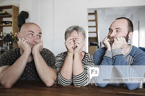 Porträt von erwachsenen Söhnen mit älterer Mutter  die zu Hause mit dem Kopf in der Hand am Tisch sitzt