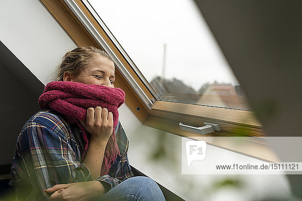 Glückliche junge Frau mit Schal am Fenster
