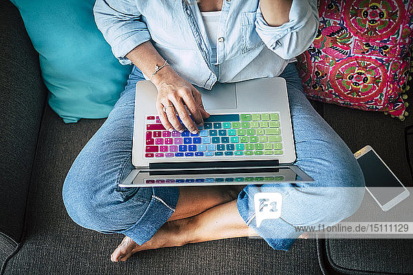 Frau benutzt Laptop mit mehrfarbiger Tastatur auf der Couch zu Hause