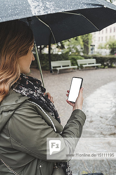 Junge Frau benutzt Handy an einem regnerischen Tag