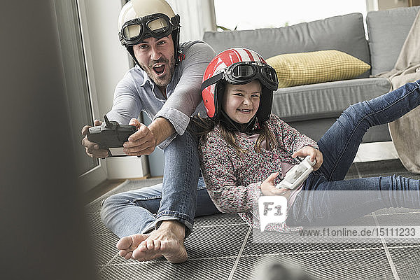 Junger Mann und kleines Mädchen tragen Bikerhelme  spielen Rennspiel mit Spielkonsolen
