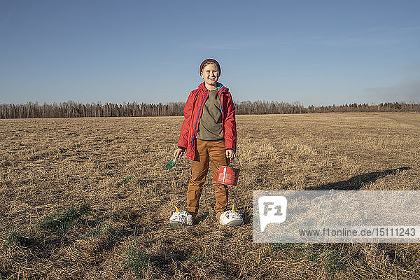Portrait of smiling boy with paint bucket and brush wearing unicorn slippers in steppe landscape