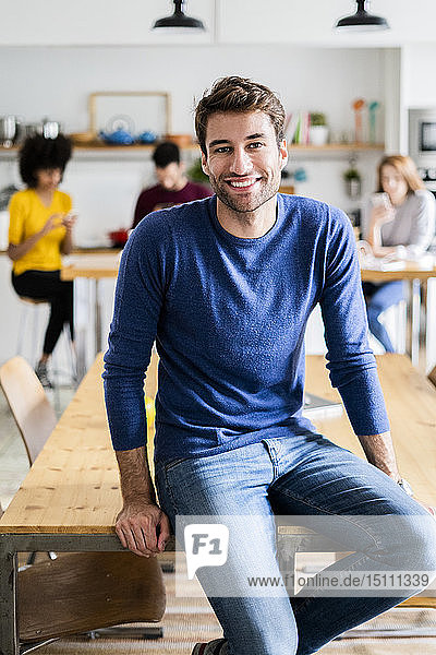 Porträt eines lächelnden Mannes am Esstisch zu Hause mit Freunden im Hintergrund
