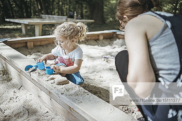Mother playing with little daughter in sandbox on a playground