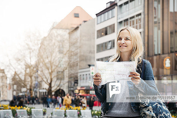 Portrait of smiling blond woman with map and baggage in the city  Munich  Germany