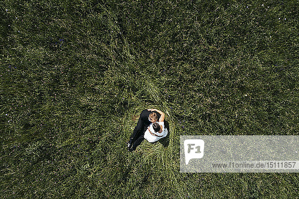 Aerial view of pregnant bride with her husband sitting on a meadow
