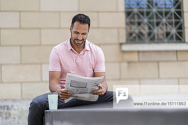 Mann mit Kaffee zum Mitnehmen liest Zeitung in der Stadt