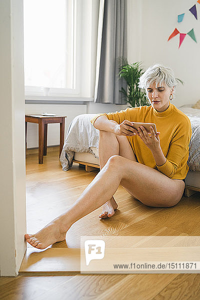 Frau sitzt zu Hause neben dem Bett und benutzt ein Mobiltelefon