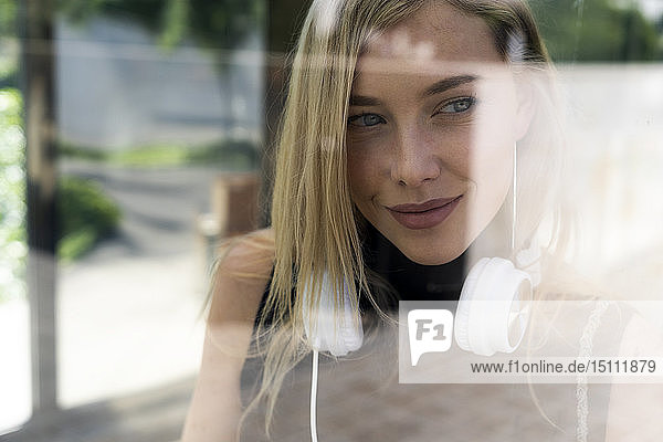 Porträt einer lächelnden blonden Frau mit Kopfhörer hinter einer Fensterscheibe