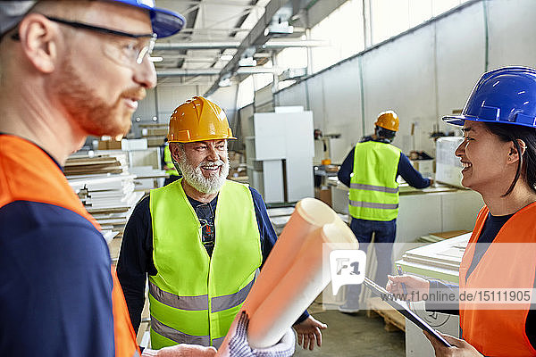 Glückliche Kollegen in Arbeitsschutzkleidung im Gespräch in der Fabrik