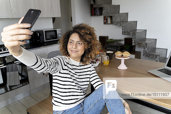 Zu Hause sitzende Frau mit Smartphone-Selfie