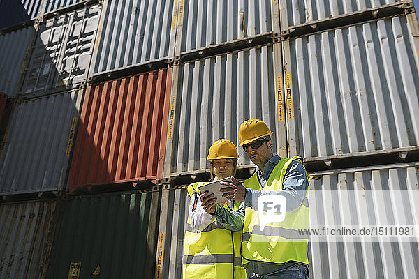 Arbeiter benutzen Tabletten vor Frachtcontainern auf einem Industriegelände