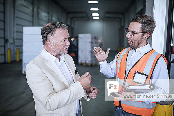 Businessman and man in reflective vest talking in industrial hall