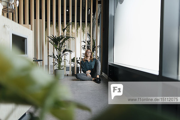 Geschäftsfrau  die in einem modernen Büro auf dem Boden sitzt