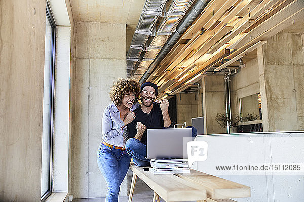 Aufgeregter Mann und Frau mit Laptop im modernen Büro