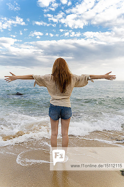 Back view of redheaded young woman standing at seafront with arms outstretched