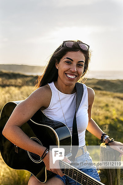 Porträt einer lächelnden jungen Frau mit Gitarre in den Dünen